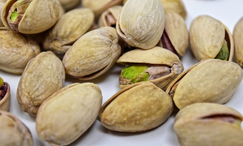 Pile of pistachios in shell on white surface