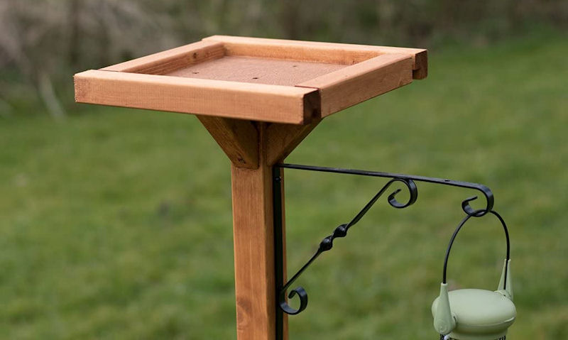 Wooden open bird table top seen with hanging bird feeder bracket