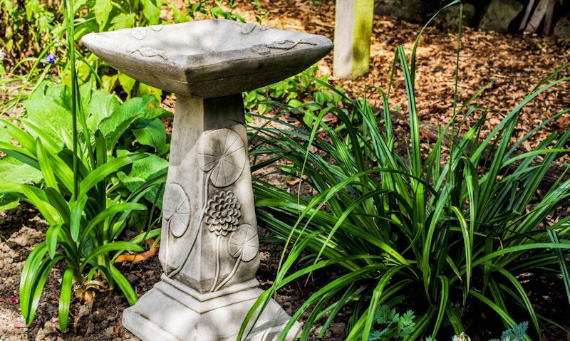 Stone bird bath sited on soil patch