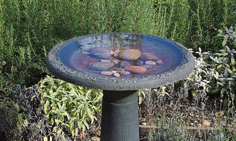 Pedestal stone cast bird bath with pebbles submerged under water in bowl